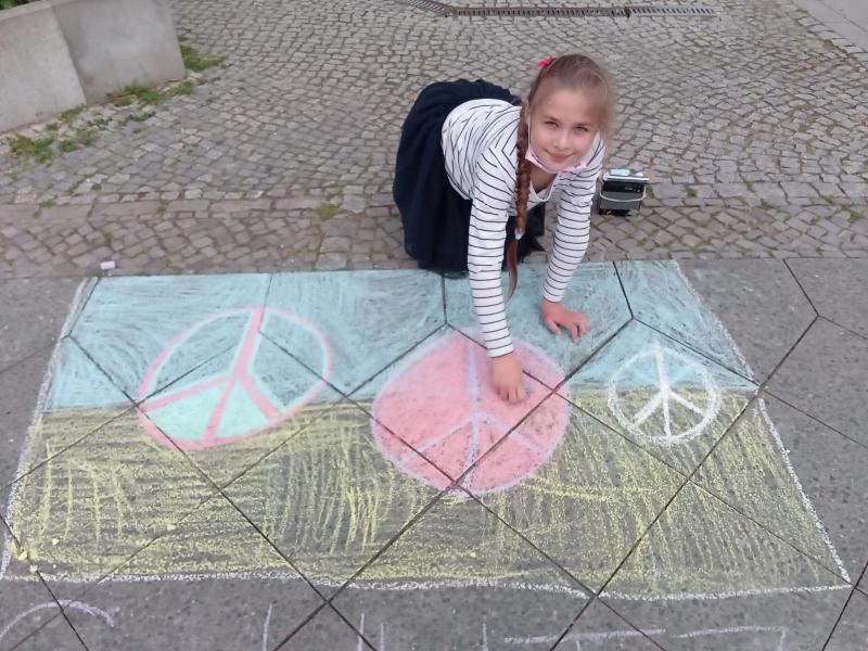 ein Mädchen malt mit Straßenkreide den Bürgersteig bunt