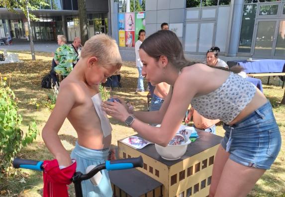 eine Helferin bringt ein Klebetattoo bei einem jungen auf