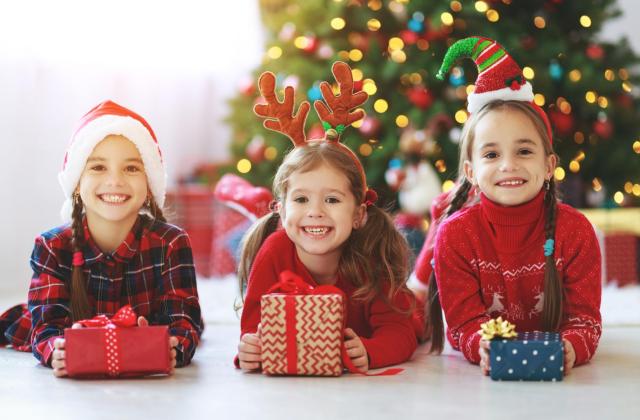 Lachende Kinder mit Geschenken vor Weihnachtsbaum