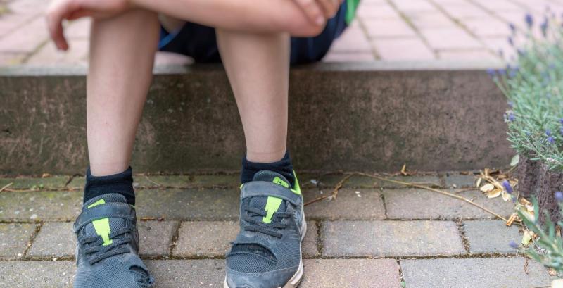 neue Schuhe sind nicht bezahlbar für armutsgefährdete Familien ein Junge mit kaputten Schuhen auf einer Treppe