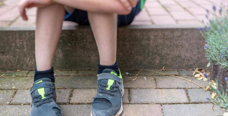 ein Junge mit kaputten Schuhen auf einer Treppe